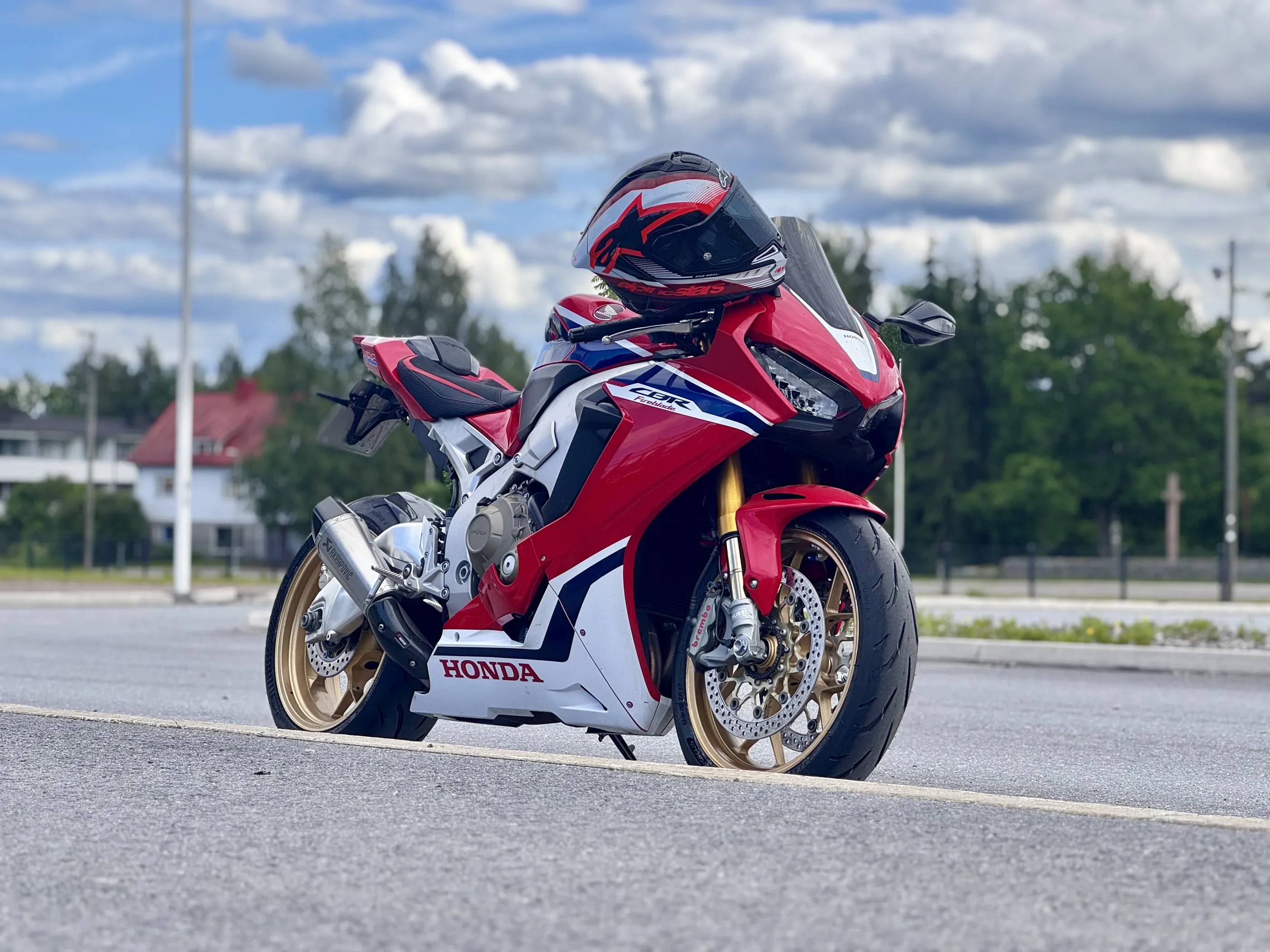 Punainen Honda CBR -moottoripyörä kypärällä pysäköitynä asvaltille pilvisen taivaan alla.