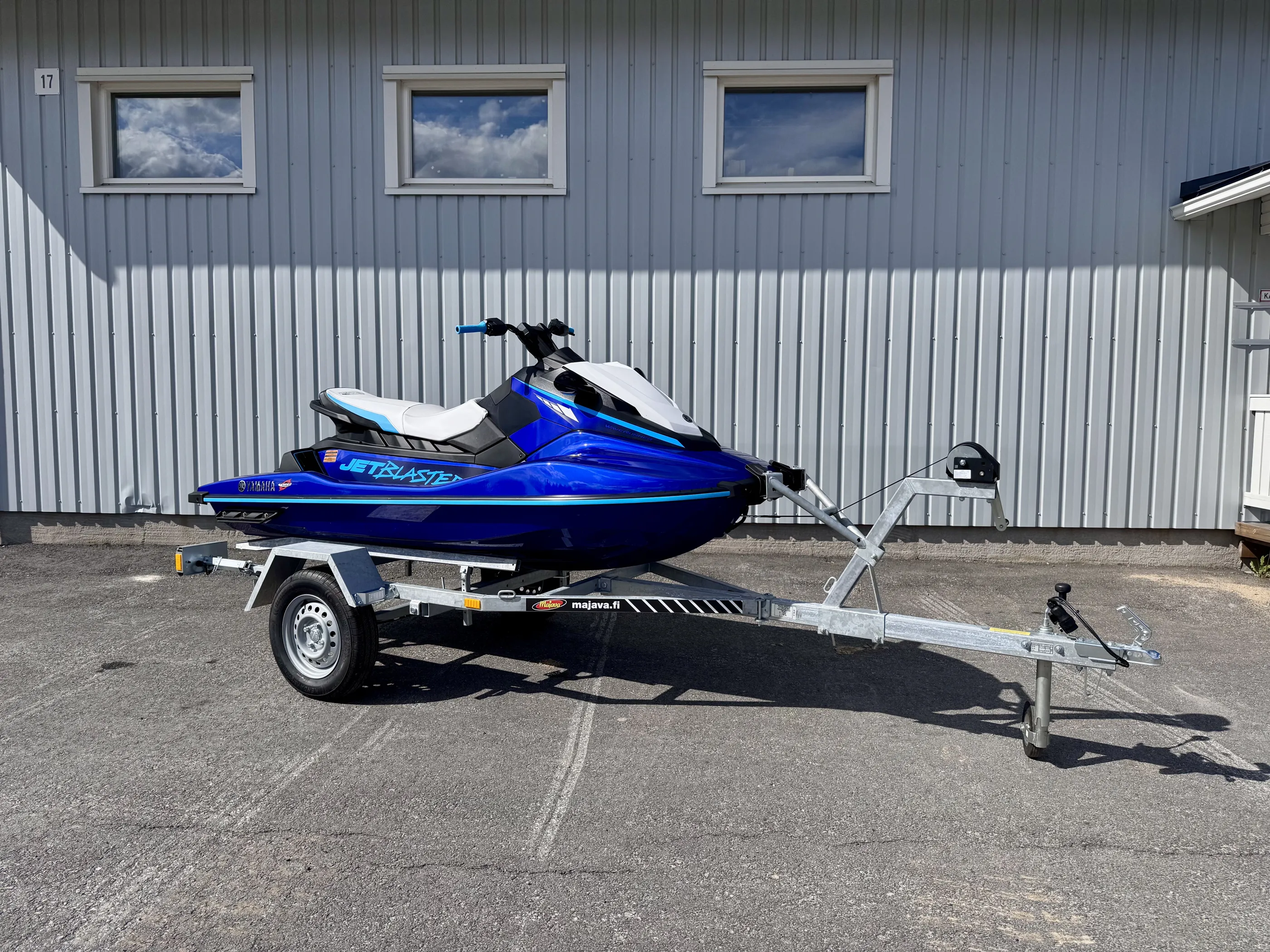 Sininen Yamaha Jet Blaster -vesijetti trailerilla harmaata seinää vasten, jossa on kolme ikkunaa ja numero 17.
