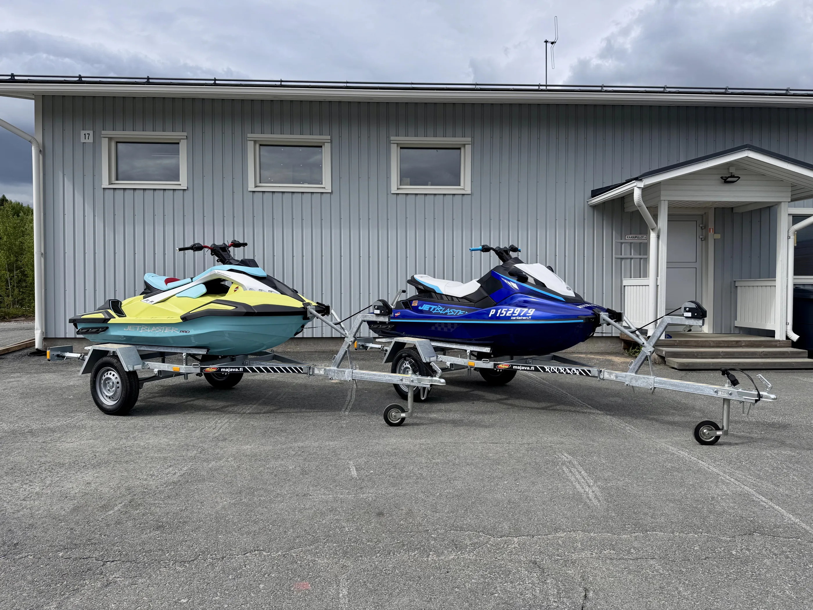 Kaksi vesiskootteria peräkärryillä rakennuksen edessä, harmaa taivas.